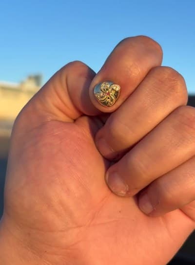 Carved gold nail cap with a red stone